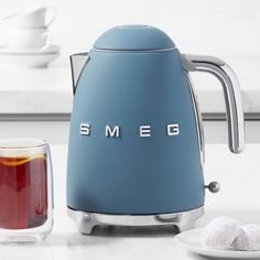 a blue smeg kettle sitting on top of a counter next to a cup and saucer