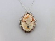 "The frame of this vintage piece is gold filigree with a wonderful, shining patina. The bright color and adorned style are the perfect compliments for this large cameo! Carved from a warm apricot hued conch shell, this lady is beautifully and classically portrayed. A white gold necklace around her throat is set with a shining diamond. This pendant does not come with the chain shown. Please feel free to contact us, we will help you find the perfect chain for your style and budget! Metal: 14K Yell Art Nouveau Cabochon Wedding Brooches, Art Nouveau Cabochon Brooches For Weddings, Formal Filigree Pendant Brooch, Art Nouveau Filigree Brooch For Collectors, Elegant Carved Brooches For Gifts, Art Nouveau Wedding Brooches With Filigree, Collectible Art Nouveau Filigree Brooches, Antique Filigree Brooch For Formal Occasions, Antique Filigree Brooches For Formal Occasions