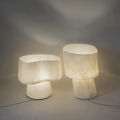 two white lamps sitting next to each other on top of a gray surface with light coming from them