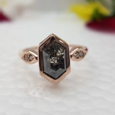 a close up of a diamond ring on a white surface with flowers in the background