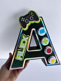 a hand holding up a sticker shaped like the letter a with game controllers on it