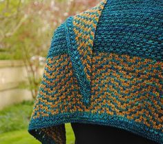 a woman wearing a blue and orange knitted shawl on top of a green lawn