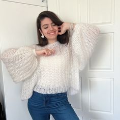 a woman is posing in front of a door wearing jeans and a white sweater with bell sleeves