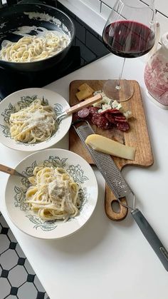 three plates of pasta with cheese and meat on the counter next to a glass of wine