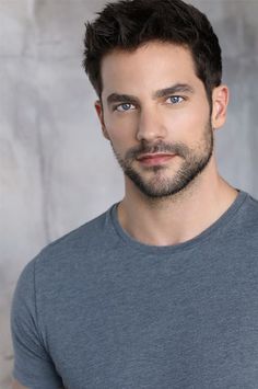 a close up of a person with a beard and blue eyes wearing a gray shirt