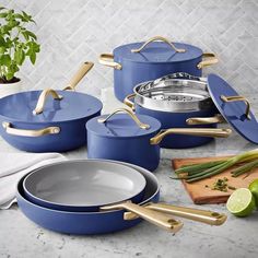 blue pots and pans with gold handles on a marble countertop next to green plants