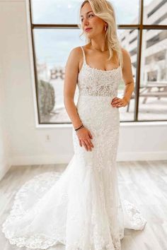 a woman standing in front of a window wearing a white wedding dress with lace on it