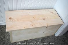 a wooden box sitting on the floor in front of a white wall and carpeted floor