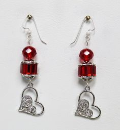 pair of earrings with red glass beads and silver heart pendants on white background, closeup