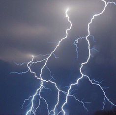 lightning strikes across the night sky over trees and land in front of a dark cloudy sky