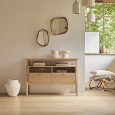 a wooden table sitting in front of a window next to a white vase and mirror