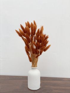 a white vase filled with brown flowers on top of a wooden table