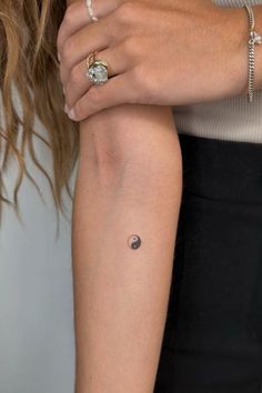 a woman's arm with a small saturn tattoo on the left side of her arm