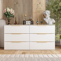 a white dresser sitting next to a window with flowers on top of it in front of a wooden wall