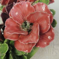 red flowers with green leaves in vase on white tableclothed surface, closeup