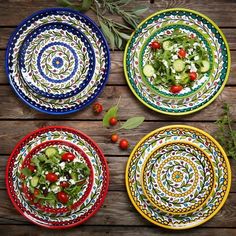 four plates with different designs on them sitting on a wooden table next to tomatoes and lettuce