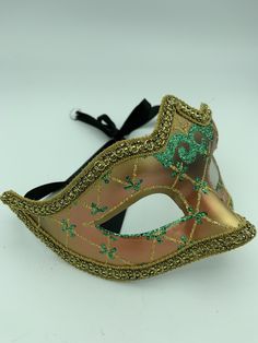 "This is a very nice original handmade and hand painted Venezia masquerade face mask made in Italy. The design on the shiny gold and orange face mask features turquoise blue and multi-color glitter with a border of gold lace and gold rope around the edges. It comes with a black ribbon tie and is stamped on the back \"Original Hand Painted Made in Italy Venezia\". The mask measures approximately 6 5/8\" long and 3 3/4\" wide and is in very good preowned condition with light wear on the back of th Green Carnival Masks And Prosthetics, Green Masks For Carnival Costume Party, Halloween Eye Mask Gift, Halloween Eye Mask As A Gift, Green Masquerade Mask For Mardi Gras, Green Mask For Masquerade Carnival, Green Masquerade Mask For Mardi Gras Party, Green Masks For Masquerade Carnival, Green Masks For Carnival Masquerade