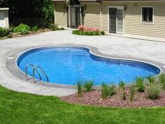 an above ground pool surrounded by grass and flowers in front of a house with landscaping