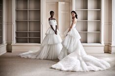 two women in wedding gowns standing next to each other on the carpeted floor