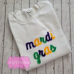 Looking for a new trendy shirt to wear this Mardi Gras? The lettering is embroidered onto a heavy weight unisex Gildan tee or Gildan Sweatshirt with a commercial embroidery machine. *Washing instructions-please wash and dry fringe shirt inside a delicate garment bag to guarantee the longevity of the item. Each time the shirt is washed the fringe becomes more fluffy. All items are custom made here at Lilly Pie Creations Mardi Gras Embroidery, Crew Neck T-shirt With Letter Embroidery For College, Embroidered Text T-shirt For College In Fall, White Machine Embroidered Tops For Streetwear, Crew T-shirt With Letter Embroidery For College, College Crew T-shirt With Embroidered Text, College Crew T-shirt With Letter Embroidery, College T-shirt With Letter Embroidery, Multicolor Embroidered Logo Tops For Fall