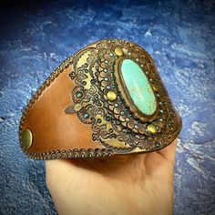 a hand holding a brown leather cuff with a turquoise stone in it