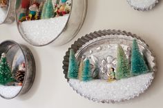 three metal plates with miniature trees on them and snow around the edges, hanging on a wall