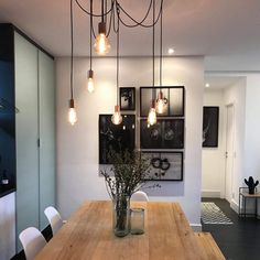 a wooden table topped with a vase filled with flowers next to lights hanging from the ceiling