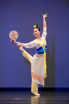 a woman is dancing on stage with her arms in the air while holding a fan