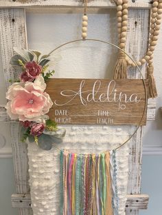 a wooden sign hanging from the side of a white door with flowers and tassels on it