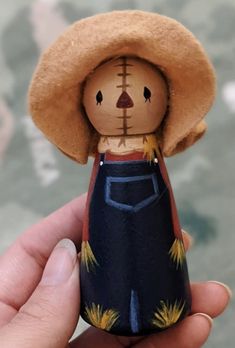 a hand holding a small wooden doll in it's right hand and wearing a straw hat