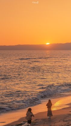 two people walking on the beach at sunset