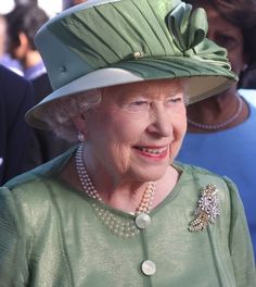 an older woman wearing a green hat and pearls on her head with other people in the background