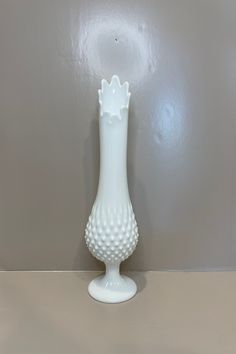 a white vase sitting on top of a table next to a gray wall and floor