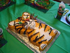 a tiger cake sitting on top of a table next to cupcakes and napkins