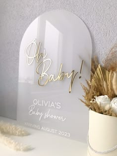 a white vase with dried flowers in it next to an acrylic sign that says oh baby