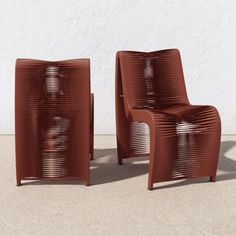 two brown chairs sitting next to each other in front of a white wall and cement floor