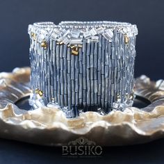 a glass candle holder sitting on top of a silver plate with gold trimmings