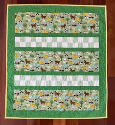 a green and white quilt with animals on it sitting on a wooden floor next to a wood floor