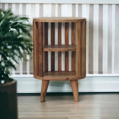 a small wooden shelf next to a potted plant on a hard wood floor in front of a striped wall