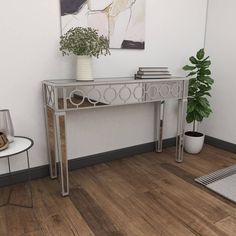 a silver console table sitting on top of a hard wood floor next to a potted plant