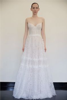 a woman standing in front of a white wall wearing a wedding dress with spaghetti straps