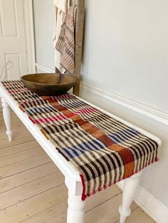 a wooden bowl sitting on top of a white bench next to a towel rack and coat rack