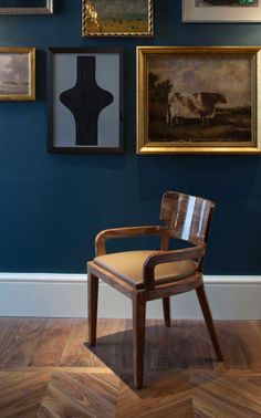 a chair sitting in front of some paintings on the wall and wooden parquet floor