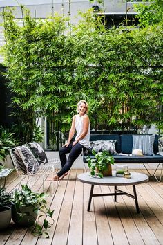 a woman sitting on top of a wooden floor next to a couch and table with potted plants