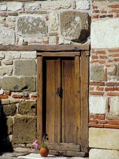 an old wooden door in front of a stone building with potted flowers on the ground