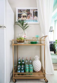 a gold bar cart with drinks and fruit on it in front of a white curtain