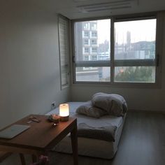 a small room with a bed, desk and large window in it's corner