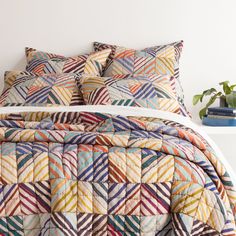 a bed with multicolored quilts and pillows on it next to a plant