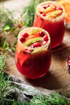 two glasses filled with fruit and garnish sitting on top of a wooden table