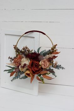 a flower arrangement in a basket hanging on a white wall with wood planks behind it